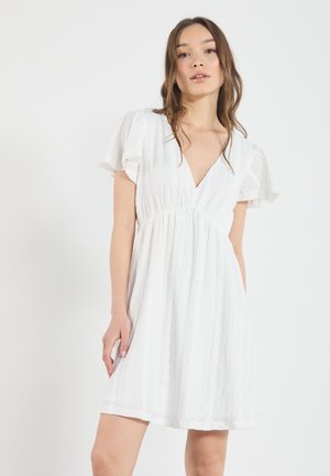 Robe blanche avec un décolleté en V, des manches courtes flottantes, un tissu texturé et une taille froncée, tombant au-dessus du genou avec une coupe décontractée.