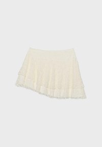 Mini-jupe blanche en dentelle superposée avec ourlet asymétrique et motif floral délicat sur un fond uni clair.