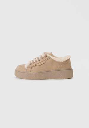 Beige suede sneaker with faux fur trim, textured platform sole, and round toe. Features beige laces and detailed stitching accents.