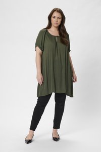 Tunique fluide vert olive avec des manches courtes et un col rond. Assortie à un pantalon noir ajusté et des escarpins noirs à bouts pointus.