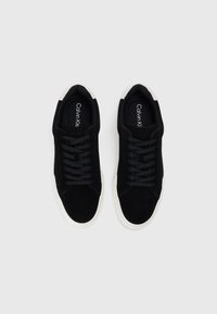 Adidași negri cu partea superioară din suede și țesătură, talpă de cauciuc albă, șireturi plate, guler căptușit și logo embossat pe talpa interioară.