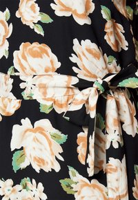 Květinové šaty s černým pozadím, které mají velké broskvové růže a zelené listy. Obsahují detail vázání v pase pro úpravu velikosti.