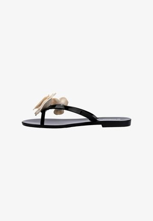 Chancla negra tipo flip-flop con un diseño elegante, que presenta una suela exterior texturizada y un adorno de flor crema en la tira.