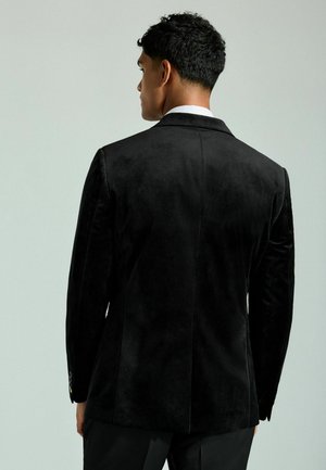 Schwarze Samtjacke mit glatter Textur, ausgestattet mit einem Reverskragen, einer einzelnen Belüftung und Knopfdetails an den Manschetten. Rückansicht des Bekleidungsstücks dargestellt.