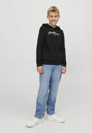Felpa nera con cappuccio e logo bianco, abbinata a jeans azzurri e sneaker bianche, progettata per abbigliamento casual giovanile.