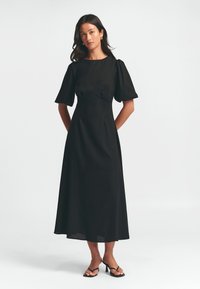 Schwarzes, knielanges Kleid mit Puffärmeln, tailliertem Oberteil und ausgestellt Rock. Glattes Material ohne sichtbare Muster oder metallische Akzente.