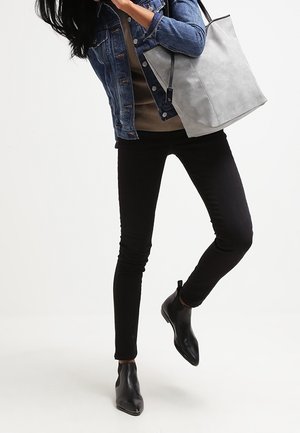 Borsa a tracolla grigia in pelle con una texture opaca, abbinata a una giacca di denim blu e jeans skinny neri. Stivali neri alla caviglia completano il look.