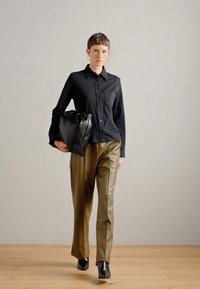 Črna srajca s gumbi in žepom, olivno zelene hlače visoko pasu ter črna usnjena torba. Hlače imajo gladko teksturo in rahlo sijaj.