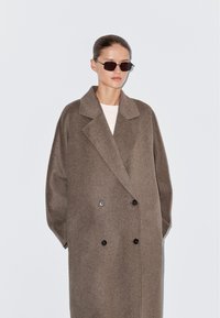 Dubbelgeknoopte bruine wollen jas met een gekarteld kraag en grote, zwarte knopen. Heeft een oversized pasvorm en zachte textuur.