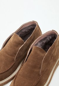 Chaussures en daim marron à enfiler avec des semelles blanches épaisses et une doublure intérieure en fourrure douce gris foncé.