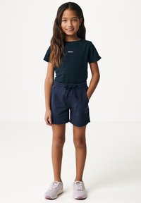 Camiseta de color azul marino oscuro con un pequeño logotipo rosa, combinada con pantalones cortos azules marinos a juego con cintura elástica y bolsillos laterales. Zapatillas deportivas ligeras.
