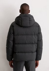 Zwarte pufferjack met een capuchon, voorzien van een gewatteerd design en hoge kraag. Het materiaal lijkt glad en waterafstotend, ideaal voor koud weer.
