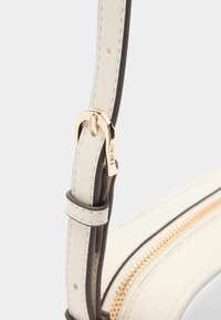 Valkoinen nahkainen laukkuhihna ruskeilla yksityiskohdilla, jossa on kiiltävä kultainen solki. Sujuva pinta, jossa näkyvät ompeleet ja vetoketjuyksityiskohta.