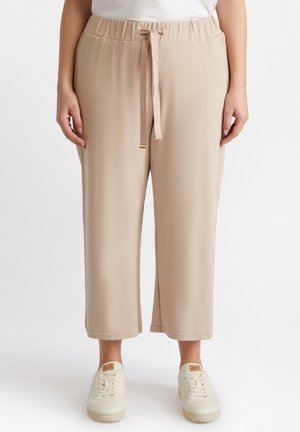 Pantaloni beige, leggeri, a vita alta con cordoncino. Presentano spacchi laterali e una vestibilità rilassata e cropped. Abbinati a sneakers bianche.