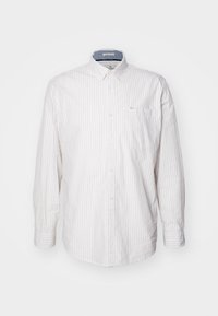 Biała koszula z długim rękawem i kołnierzykiem, w jasne pionowe paski, zapinana na guziki, z jedną kieszenią na piersi oraz wewnętrznym akcentem denimu przy kołnierzyku.
