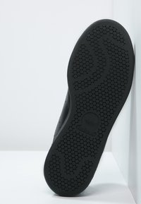 Svart sneakersula med ett strukturerat bikakemönster, en böjd design och präglat logotyp. Släta kanter och hållbart material synligt.