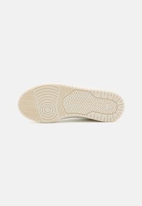 Suola di sneaker con un design in gomma testurizzata di colore bianco sporco, caratterizzata da motivi circolari e zigzag per garantire aderenza e presa.