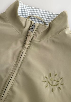 Helle Olivfarbe, mit Reißverschluss, Jacke mit hohem Kragen und innenseitigem Futter im Karomuster; verfügt über ein gesticktes Sonnenmotiv auf der Vorderseite.