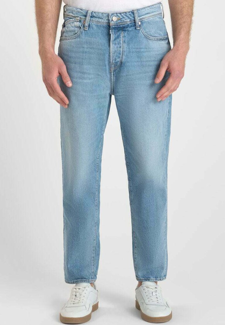 Vaqueros de mezclilla azul claro con corte recto, textura desgastada, diseño de cinco bolsillos y cierre de botón. Llevados con zapatillas blancas.