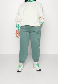 Ljust färgad oversized sweatshirt, gröna joggingbyxor med logodetalj och silverfärgade träningsskor med gröna accenter. Outfiten har en avslappnad passform.