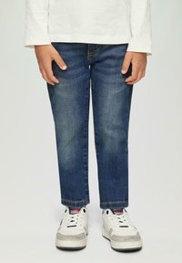 Dżinsy w ciemnoniebieskim kolorze, prosty krój nogawki z lekkim przetarciem. Połączone z białymi trampkami z szarymi akcentami i teksturowanymi detalami.