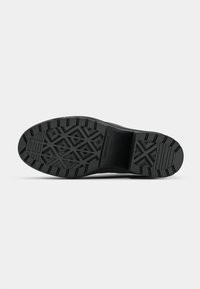 Semelle de chaussure en caoutchouc noir avec une surface texturée, présentant un motif géométrique et des rainures profondes pour une meilleure adhérence et traction.