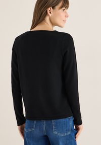 Czarna bluzka z długim rękawem o kwadratowym dekolcie i gładkiej teksturze, zestawiona z niebieskimi dżinsami z tylnymi kieszeniami i detalami w szwie.