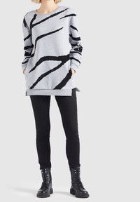 Felpa grigia con strisce astratte nere, con vestibilità rilassata, maniche lunghe, tasche laterali e orlo a costine. Abbinata a leggings neri e stivali.