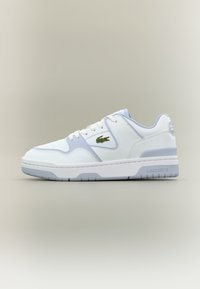 Λευκό και ανοιχτό γκρι sneaker χαμηλού ύψους με πράσινο λογότυπο κροκόδειλου στο πλάι και το σήμα "Lacoste" στη σόλα, εμφανίζεται σε προφίλ.