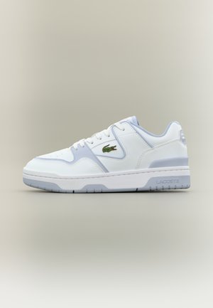 Valged ja heledat halli madala lõikega tennised rohelise krokodillilogoga küljel ning "Lacoste" brändinguga tallal, nähtud küljelt.