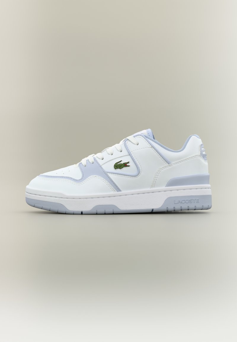 Λευκό και ανοιχτό γκρι sneaker χαμηλού ύψους με πράσινο λογότυπο κροκόδειλου στο πλάι και το σήμα "Lacoste" στη σόλα, εμφανίζεται σε προφίλ.