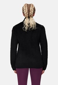 Giacca in pile nera con un motivo testurizzato, dotata di maniche lunghe e vestibilità rilassata. Indossata con leggings viola, vista da dietro.