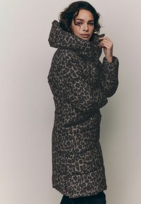 Pufasta jakna s uzorkom leopard printa u tamnosmeđoj i crnoj boji. Ima visoki ovratnik, džepove na zatvarač i kviltanu teksturu.