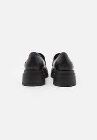Zwarte leren schoenen met een rond ontwerp, verhoogde rubberen zool en opvallende gouden accenten. Soepele textuur, minimale zichtbare stiksels.