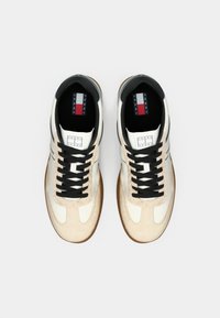 Sneakers with a beige suede and white leather upper, black laces, black lining, and brown rubber sole. Features logo on tongue.