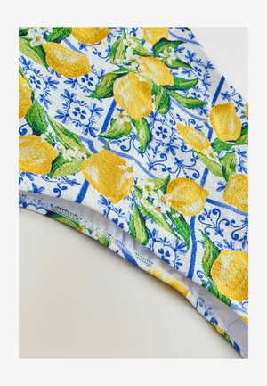Tissu à motifs présentant de grands citrons jaunes et des feuilles vertes sur un fond en carrelage bleu et blanc. Surface texturée avec un bord élastique.