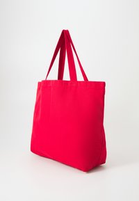 Red fabric tote bag with two red fabric straps, rectangular shape, smooth texture, and minimalistic design. No visible hardware or patterns.