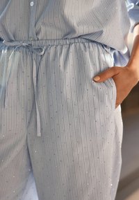 Niebieski zestaw piżamowy w paski, wykonany z miękkiego materiału, z wertykalnymi paskami i małymi błyszczącymi akcentami, z elastycznym paskiem w talii i bocznymi kieszeniami.