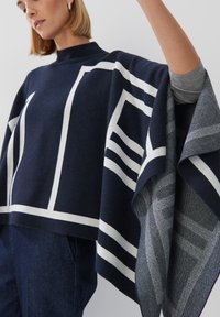 Marineblauer Poncho mit kontrastierenden weißen geometrischen Linien; aus einem weichen Stoff gefertigt. Verfügt über einen hohen Kragen und ein drapiertes Design.