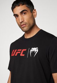 Sort bomulds T-shirt med rødt UFC-logo og hvid slange grafik på fronten. Korte ærmer og rund halsudskæring. Klassisk pasform.