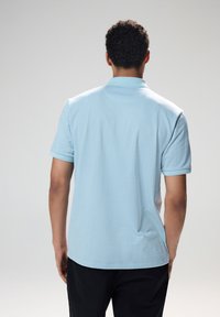 Polo shirt azzurro chiaro con un motivo testurizzato, maniche corte e colletto. La parte posteriore presenta un orlo dritto e sottili spacchi laterali.