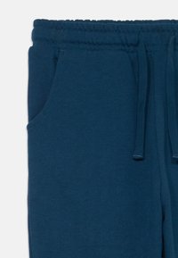 Sötétkék jogging nadrág, puha tapintással, rugalmas derékpánttal, zsinórral állítható záródással és oldalsó zsebekkel. Nincs látható minta vagy fém kiegészítő.