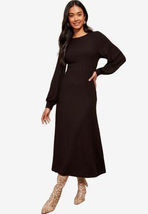 Zwarte geribde lange mouw jurk met een aansluitende taille en een lange rok, gecombineerd met gebroken slangenprintlaarzen. Eenvoudige ronde halslijn.