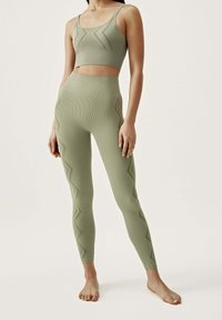 Olive green activewear set featuring a cropped top with geometric ribbed design and high-waisted matching leggings with zigzag patterns.