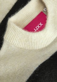 Maglione in lana a strisce crema e nere con scollo a costine. Etichetta interna in rosa brillante con il testo "JJXX", che mette in evidenza una consistenza morbida.