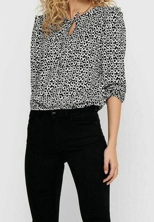 Black and white floral long-sleeve blouse with a keyhole neckline, paired with high-waisted black pants.