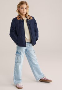 Chaqueta de plumas azul marino con cuello de estampado de leopardo, suéter crema, pantalones cargo azul claro y zapatillas rosas con acentos marrones.