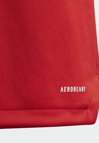 Tela roja con un acabado texturizado, que presenta un logotipo "AEROREADY" en la esquina inferior derecha.