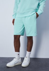 Pantalones cortos deportivos en un tono azul claro, confeccionados con una tela suave, que cuentan con una cinturilla elástica y bolsillos laterales, combinados con zapatillas blancas y calcetines.