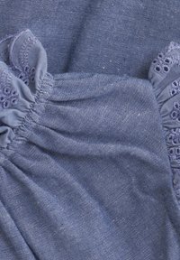 Blå bomullstyg med samlad textur och spetsdetaljer längs kanterna, med en subtil glans och små broderade blommor.